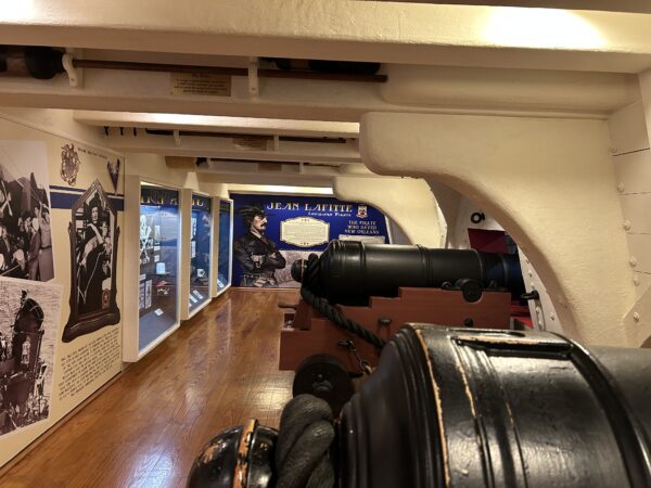 A view of the exhibit looking down the deck, including a pair of replica cannons and some display cases with artefacts inside.