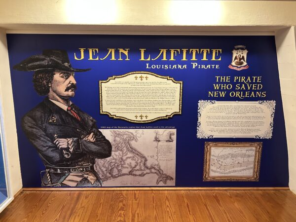 A wall display describing the history of Louisiana pirate Jean Lafitte. Classic art depicts Lafitte as a surly looking man dressed in a dark coat and hat with his arms folded across his chest.